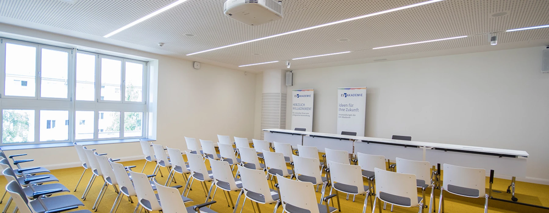 Seminarraum mit Kinobestuhlung und leerem Podium, Sicht von schräg hinten in Richtung Podium
