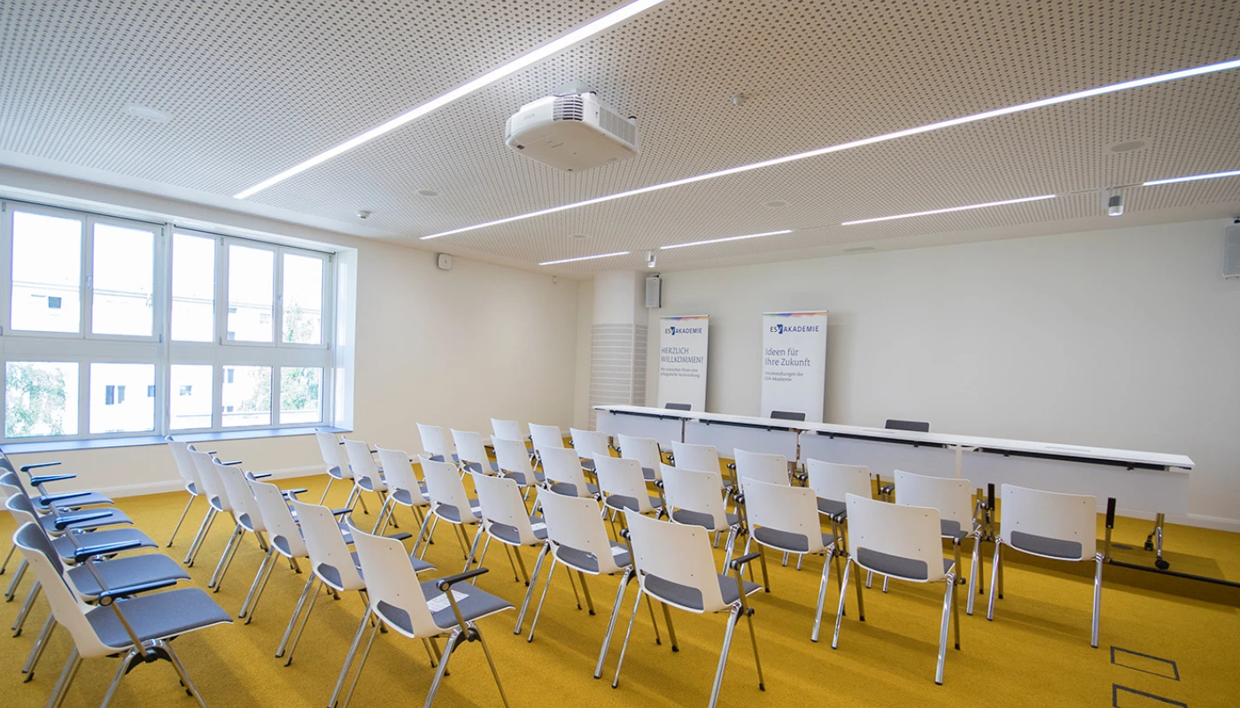 Seminarraum mit Kinobestuhlung und leerem Podium, Sicht von schräg hinten in Richtung Podium