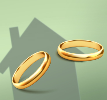 Zwei goldene Eheringe vor Haus-Silhouette – symbolisiert Ehe, Vermögensaufteilung, Zugewinnausgleich und steuerliche Gestaltung im Scheidungs- und Nachfolgekontext