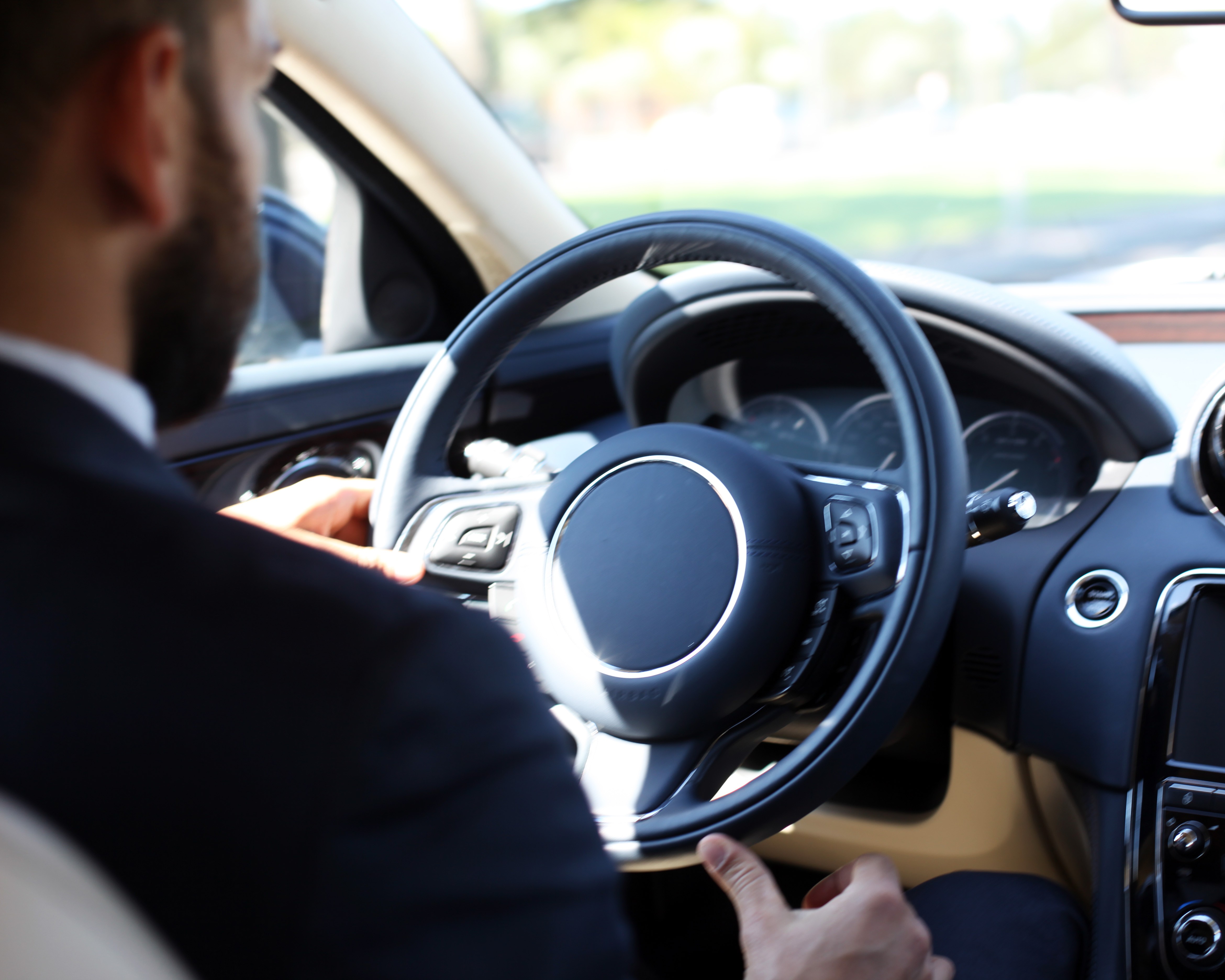 Blick aus dem Fahrzeuginnenraum auf Lenkrad, Armaturenbrett und eine Person am Steuer eines Pkw.