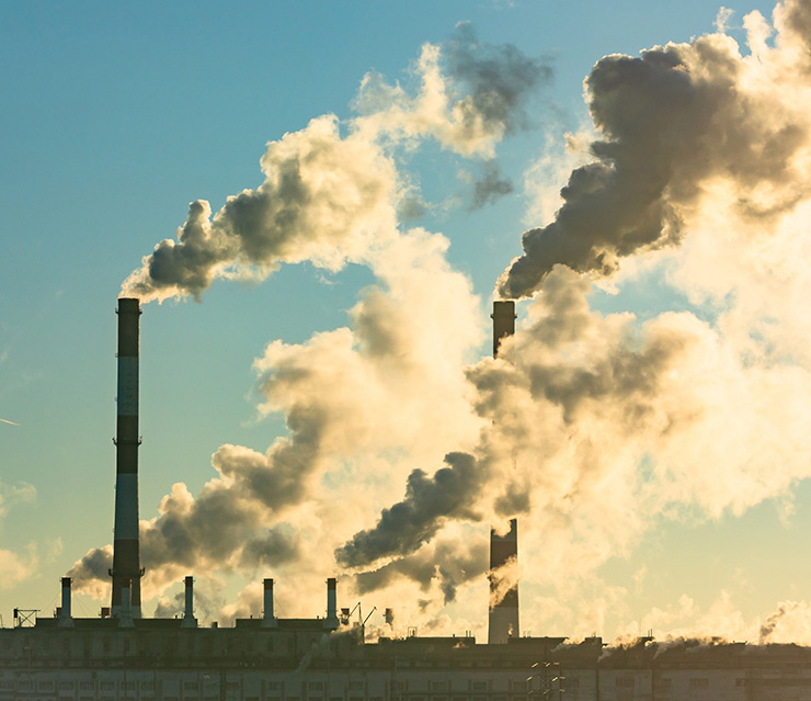 Industrieanlage mit Schornsteinen und aufsteigenden Emissionen als Symbol für den europäischen Emissionshandel und Treibhausgasemissionen.