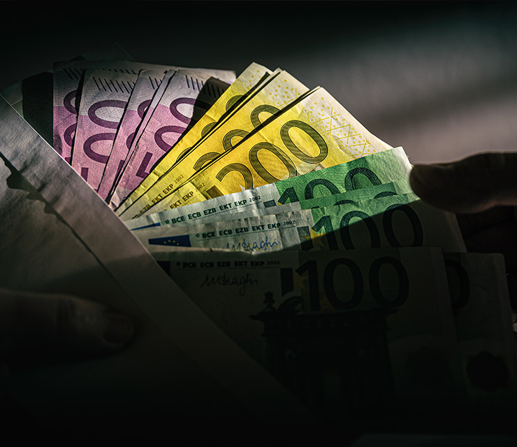 Hand übergibt Euro-Banknoten aus einem Umschlag als Symbol für finanzielle Transaktionen, Haftungsfragen und steuerrechtliche Sachverhalte.