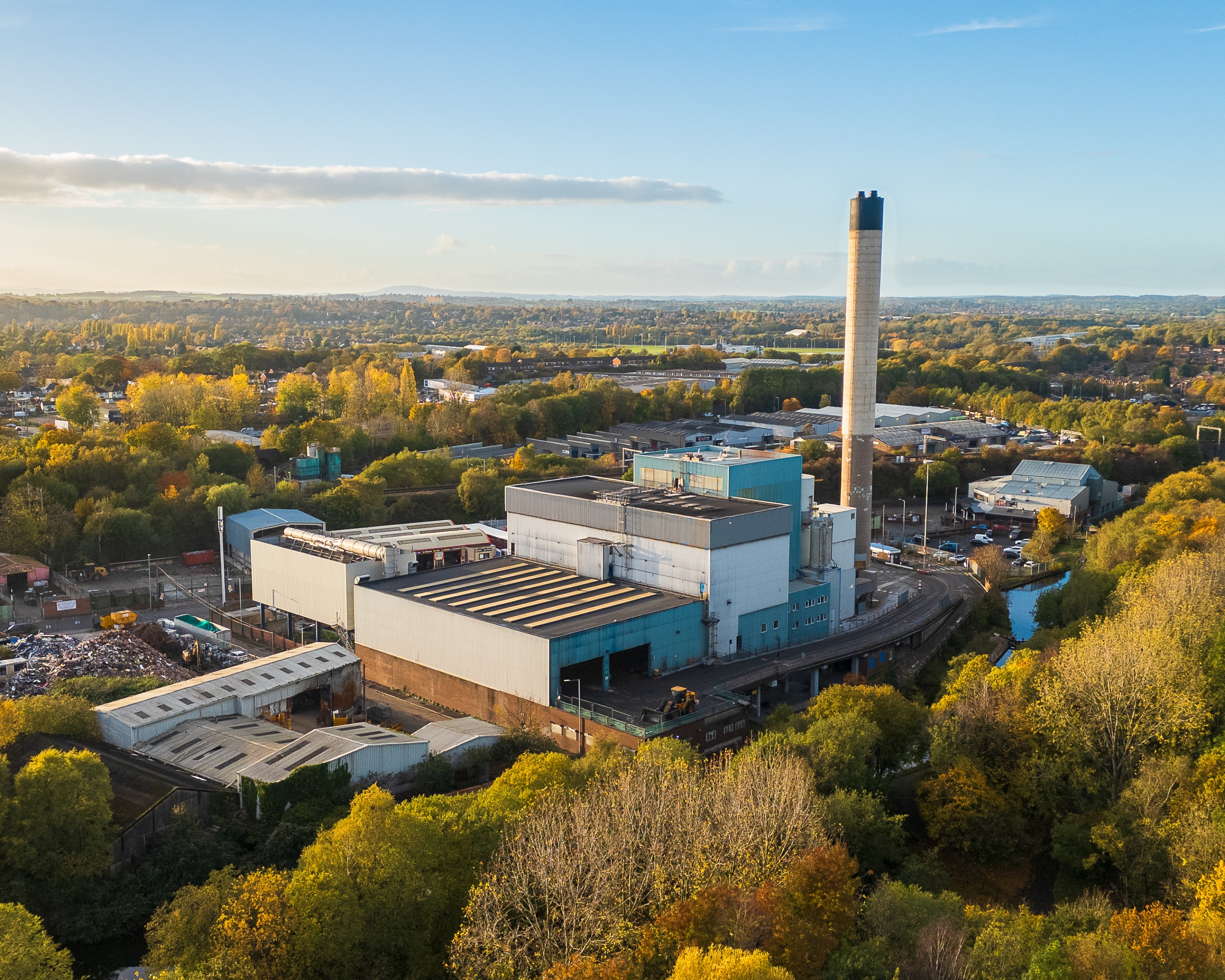Luftaufnahme einer großflächigen Müllverbrennungsanlage mit Schornstein, umgeben von Bäumen, Industriegebäuden und Verkehrswegen.