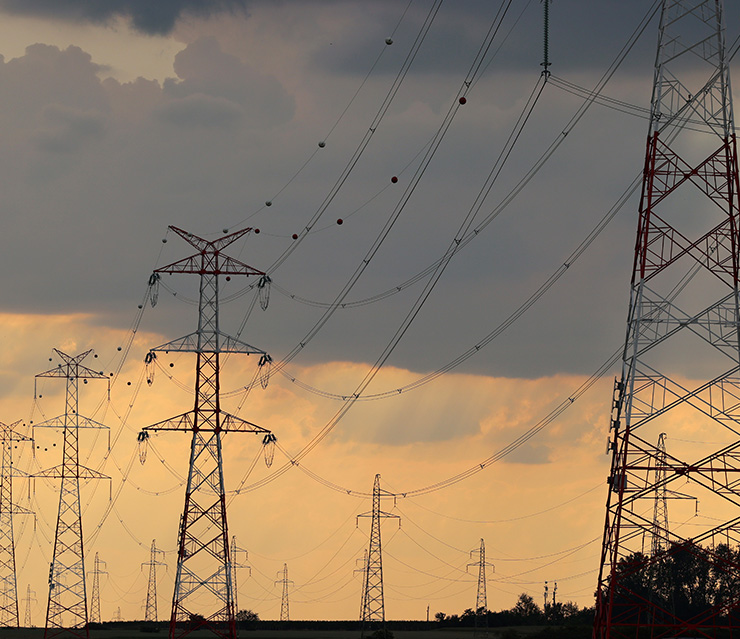 Hochspannungsleitungen und Strommasten vor bewölktem Himmel als Symbol für Energieversorgung und Grundversorgung mit Strom.